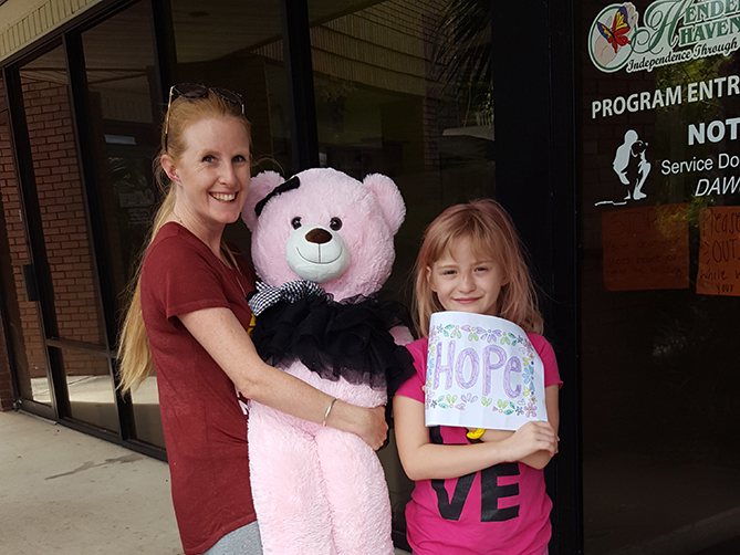 Parent holding pink teddy bear with daughter holding paper that says "hope"